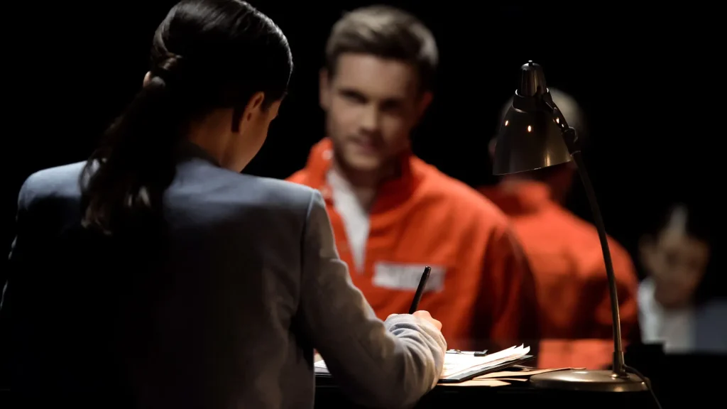 A lawyer talking to a prisoner in an orange jumpsuit.