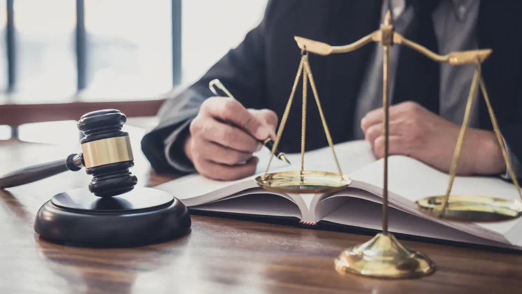 Lawyer writing in a book with scales of justice and a gavel on the desk.
